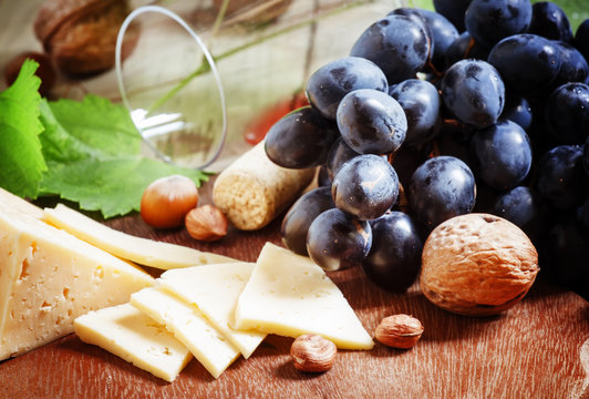 Cheese, blue grapes, vine, nuts and a glass, selective focus