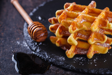 Belgian waffles with honey on a black background.