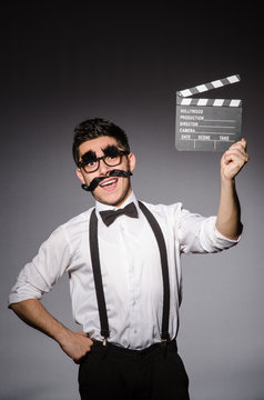 Young caucasian man with false moustache and clapperboard agains