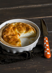 tart with cheese in a ceramic baking dish on dark wooden background
