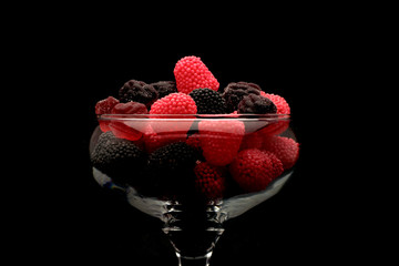 raspberries and blackberries in a beautiful glass closeup on a black background