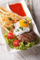 Juicy steak, a fried egg and French fries on a plate close-up. Vertical
