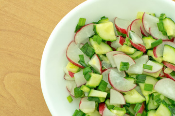 Fresh salad of cucumbers and radishes in a dish on a wooden table