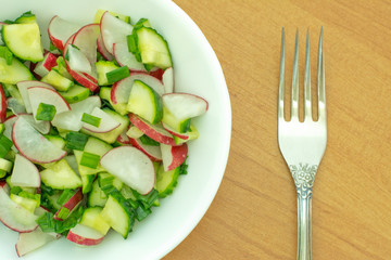 Fresh salad of cucumbers and radishes in a dish on a wooden table with fork