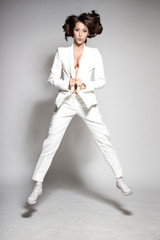 Awesome caucasian attractive joyful happy sexy dance model is jumping in studio wearing white suit on gray background © andpar