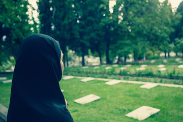 Muslim woman dressed in burqa standing on graveyard