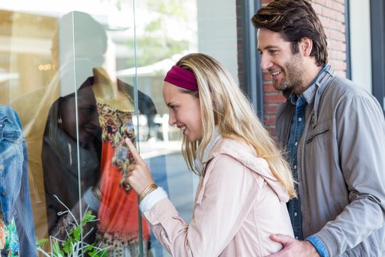 Smiling couple going window shopping and pointing at clothes