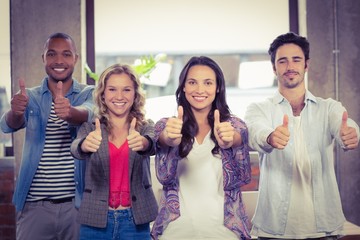 Portrait of business people giving thumbs up in office