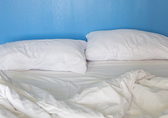 An unmade bed with white linens background blue wood