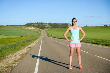 Sporty motivated woman portrait. Female athlete standing outdoor after running and exercising on countryside road.