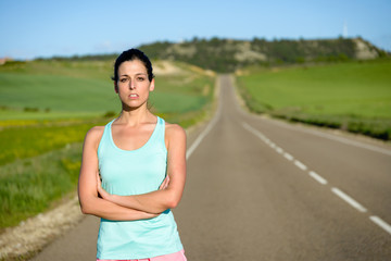 Sporty motivated woman portrait. Female athlete crossing arms after running and exercising on countryside road.