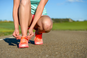 Running and sport concept. Female athlete tying sport footwear laces on road before training.