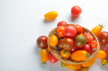 Fresh colorful tomatoes in a basket for use as cooking ingredients on white background.