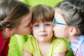 Embarrassed little girl kissed by two sisters.