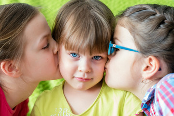Surprised little girl kissed by two sisters.