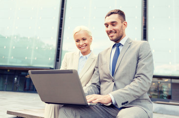 smiling businesspeople with laptop outdoors