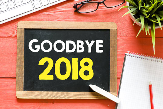 Blackboard with goodbye 2018 and chalk , keyboard,notebook,glasses and green plant on wooden background