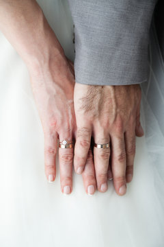 Closeup of newlyweds hands with rings against white dress