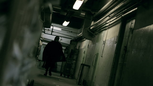 Crazy murderer in mask with sledge-hammer in his hand walking along corridor of prison 