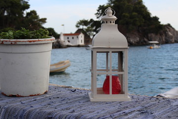 White lantern with red candle near a pot with flower