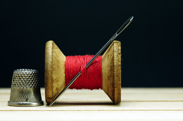 Old spool of thread with needle closeup. Tailor's work table. textile or fine cloth making.