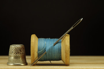 Old spool of thread with needle closeup. Tailor's work table. textile or fine cloth making.