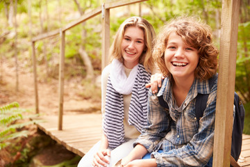 Siblings sitting on a wooden bridge in a forest, portrait