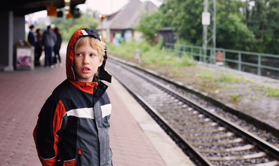 7 years old boy standing on a railway station and waiting for th