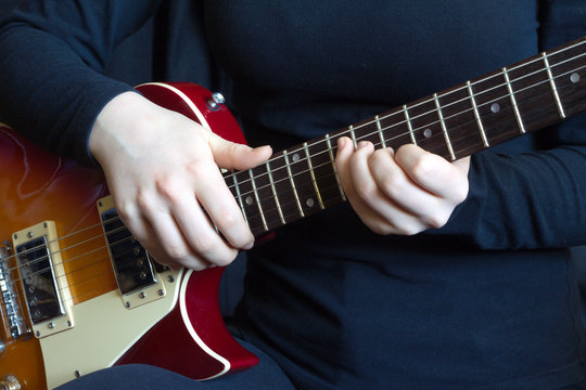 Musician in black on red six strings electric guitar playing. Hands of the musician closeup