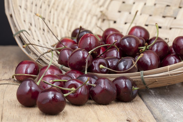 Juicy ripe cherries in bamboo basket on old wooden table top.

