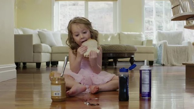 Medium shot of ballerina girl eating sandwich on floor / Cedar Hills, Utah, United States
