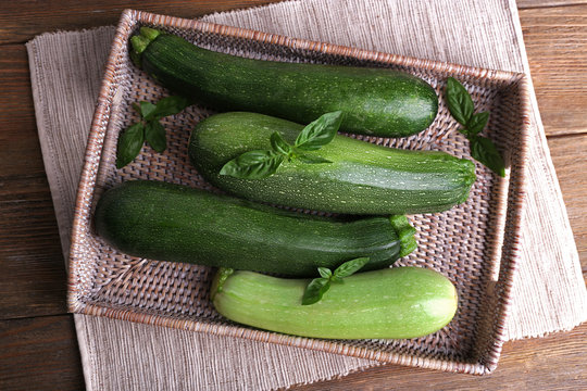 Fresh zucchini with squash and basil on wicker tray close up