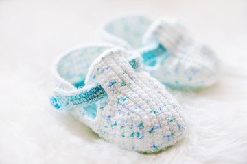 Fototapeta na wymiar Little baby shoes. Handknitted first shoes for boy or girl. Crochet handmade bootees on white fluffy background.