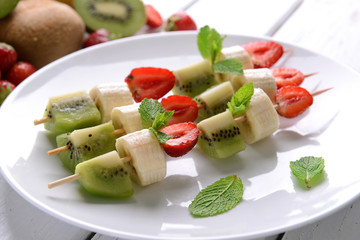 Fresh fruits on skewers in plate on table, closeup