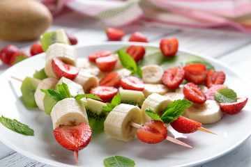 Fresh fruits on skewers in plate on table, closeup