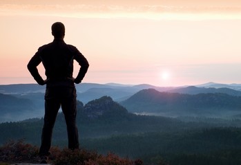 Man gesture triumph. Satisfy hiker in dark sportswear at edge with heather.Tall man on the peak of sandstone cliff watching to landscape.