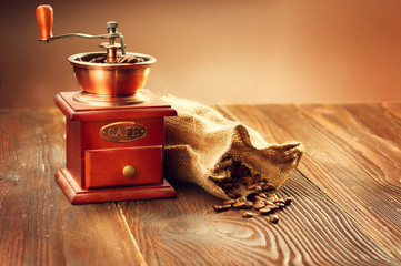 Coffee mill with burlap sack full of roasted coffee beans over wooden vintage table
