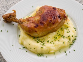 Roasted chicken leg marinated in the honey, paprika and garlic with mashed potatoes as a side dish and butter. On the top is only cutted chives. On the white plate and stone table closeup.