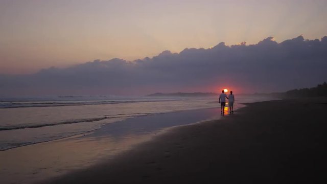 Wide slow motion shot of couple walking on beach at sunset / Esterillos, Puntarenas, Costa Rica