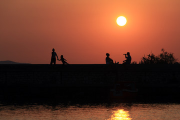 Fototapeta na wymiar Sunset Scene with People Silhouettes, Sea and Sun Road