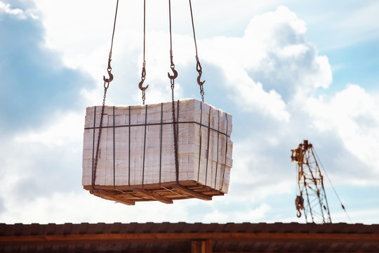 Closeup image of crane lifting heap of bricks at blue sky summer