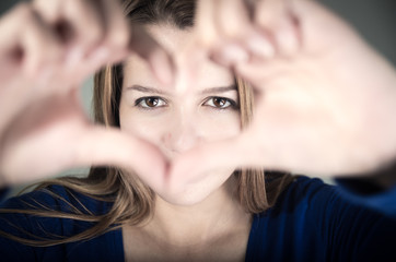 closeup portrait of cute young teen girl making a heart with