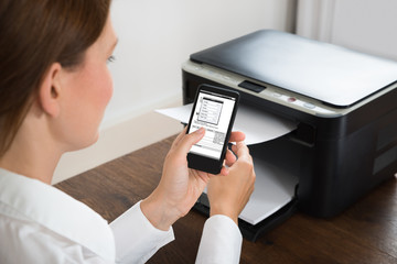 Businesswoman With Mobile Phone Connected To Printer