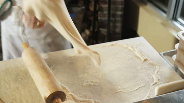man rolling out pizza dough in a pizzeria