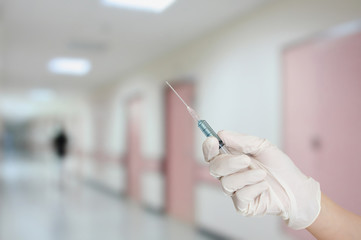 hand with protective glove injecting drug with hospital interior