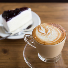 Hot coffee latte and blueberry cheesecake on wooden table.