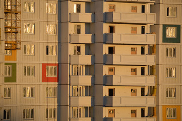 Строительство нового жилого дома. Фасад многоэтажной новостройки, освещенный лучами заходящего солнца вечером