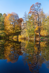 Obraz premium Trees in autumn colors on a lake with a house on a hill reflecting in water