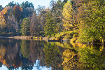 Lake with a jetty by the beach and reflections of autumn colors in the water