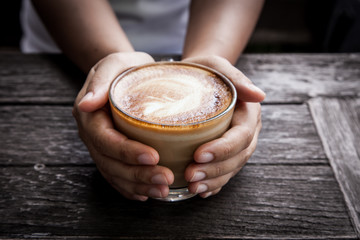 woman hand holding cup of coffee on wooden table in morning time